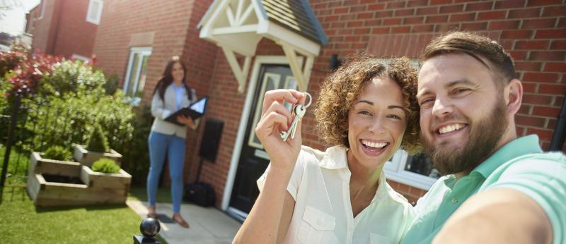 a young couple celebrate getting the keys to their new home by taking a selfie in the garden
