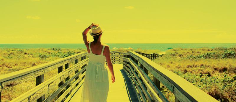 Photo of woman on a boardwalk walking towards the beach