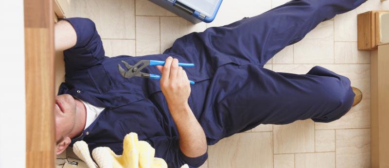 plumber with tools on floor with head under cabinet