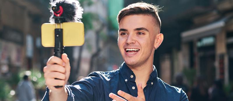Photo of a young man holding his smartphone on a tripod taking video of himself