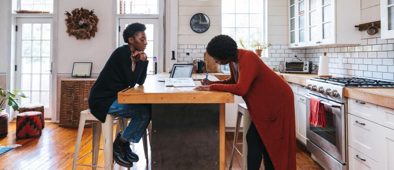 Woman signing paperwork in kitchen with another woman