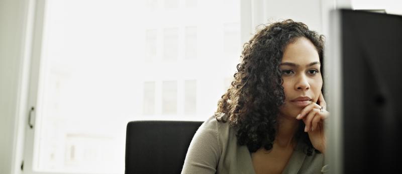 woman with hand to face in front of computer monitor