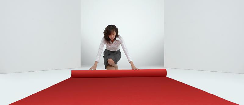 business woman rolling out a red carpet in a white room