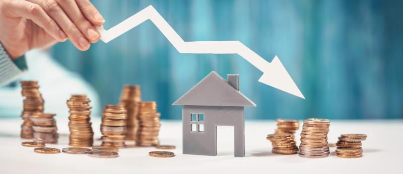 stacks of coins and a small house with a downward pointing arrow above. A hand is holding the arrow