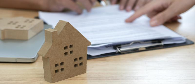 small cardboard house on desk with hands filling out paperwork