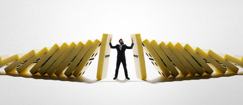 Business man standing in the middle of two sets of dominoes falling with man stopping the falling