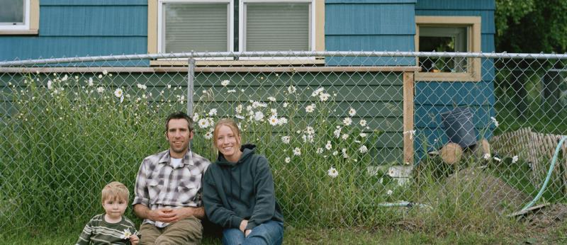 couple and child sitting in front of a chain link fence 