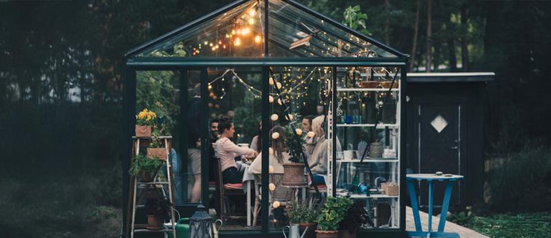 Young multi-ethnic friends enjoying dinner party in glass conservatory room at back yard 
