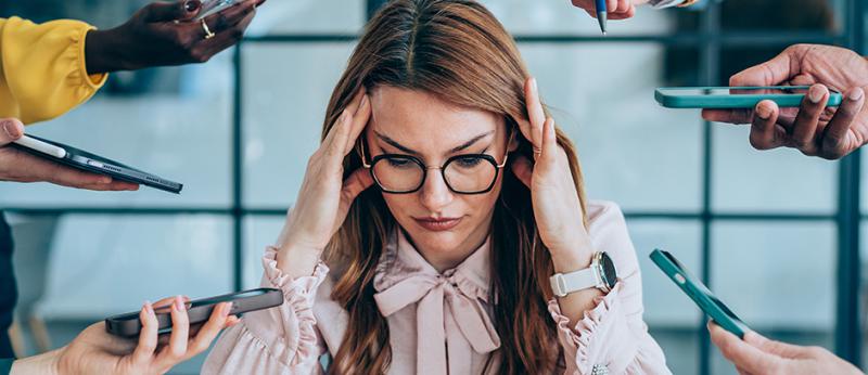 Photo of a stressed woman with hands holding many types of tech out to her