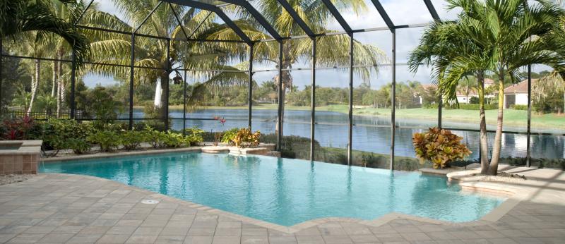 A backyard pool located in a tropical setting covered by a screen lanai. Lake in behind.