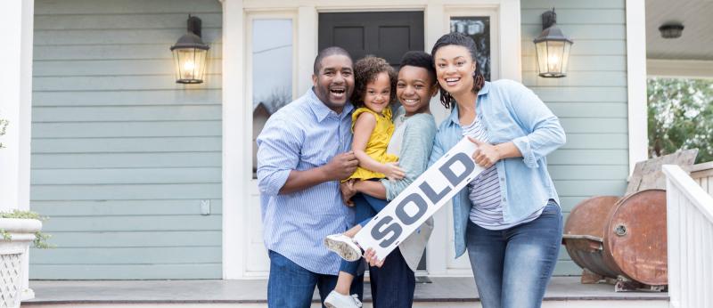 family on front porch of house holding sold sign