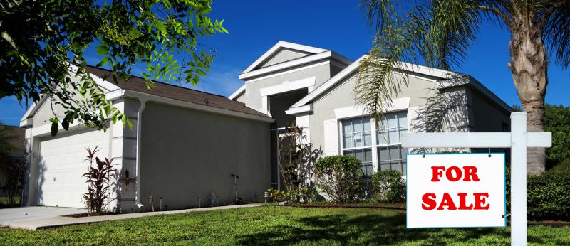 Moderate Florida home with palms trees and a for sale sign