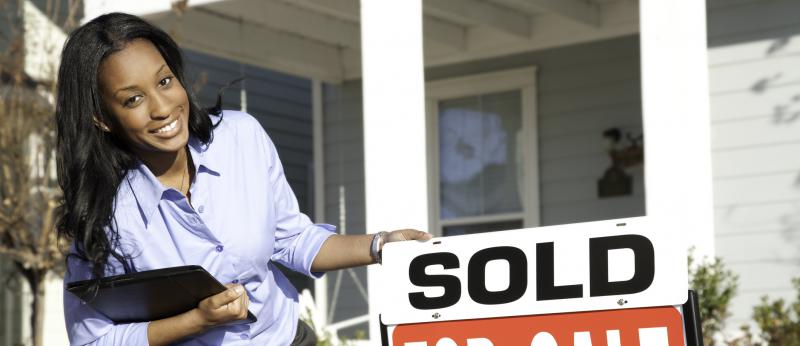 Woman smiling beside a for-sale sign with sold posted over it