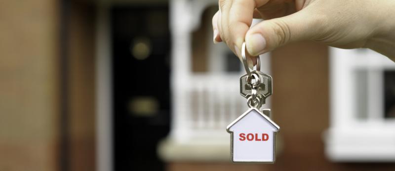 Hand in front of a house holding keychain with "sold" inside small house