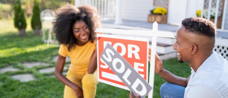 Husband and wife showing off sold sign in front of house