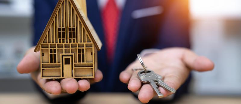 Blurry man in suit holds small house and keys in his hands