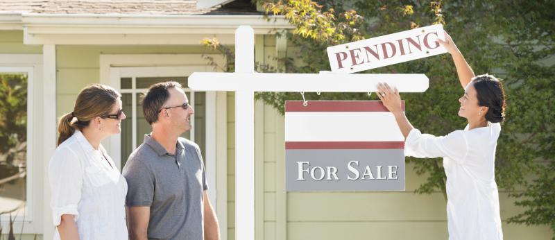 Couple watches their Realtor add a pending sign to a home's for-sale sign