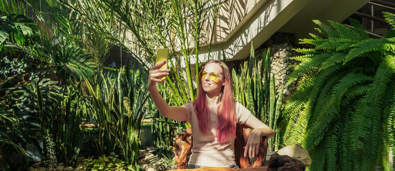 A woman taking a selfie photo amid an inside garden with trees and plants
