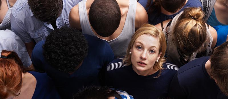 Photo of a woman looking up at the camera among man other people looking down