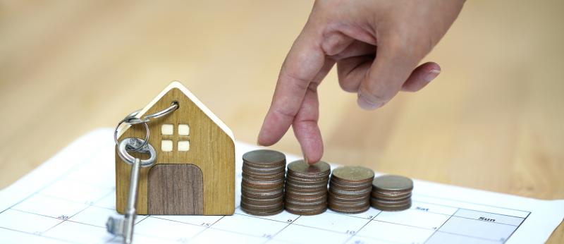small wooden house with key, hand walking on stacks of coins, all on calendar page