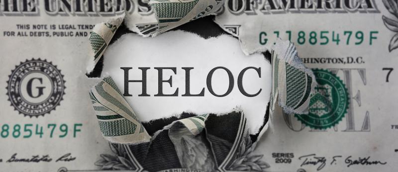 One dollar bill with a hole that says HELOC behind it