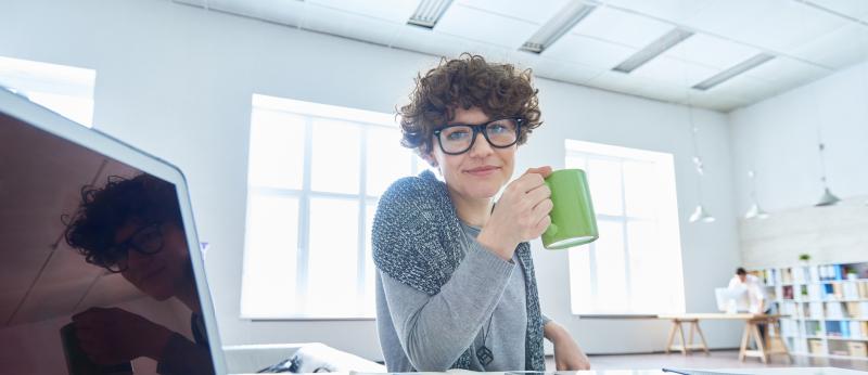 woman at computer desk holding coffee cup