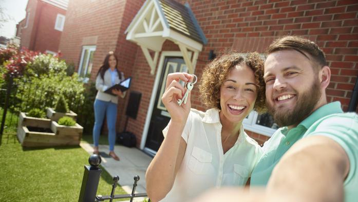 a young couple celebrate getting the keys to their new home by taking a selfie in the garden