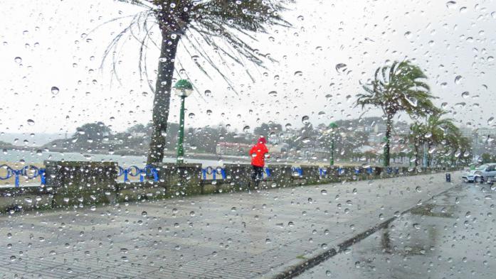 Main in red raincoat jogging in rain near beach