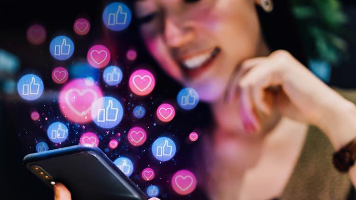 Photo of a woman looking at her phone with like symbols emanating from the phone
