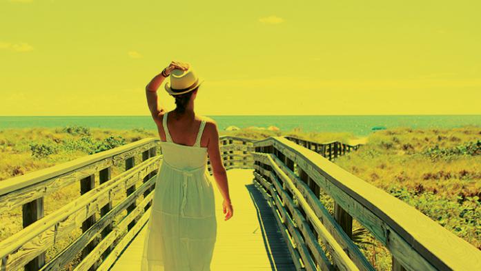 Photo of woman on a boardwalk walking towards the beach