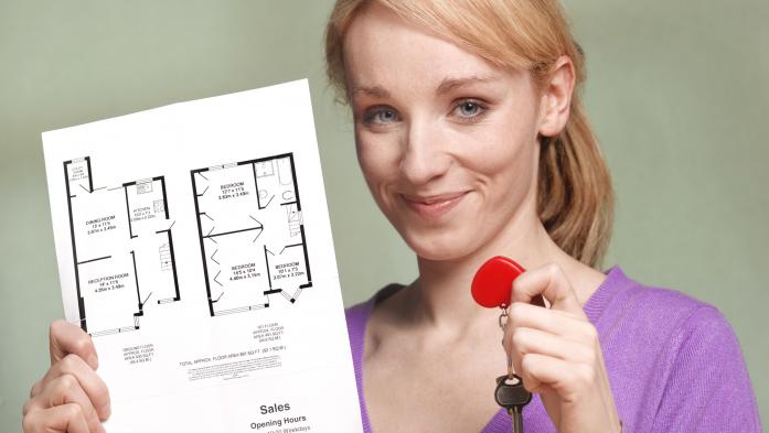 A woman holds a key in one hand and a printed copy of floor plans in the other