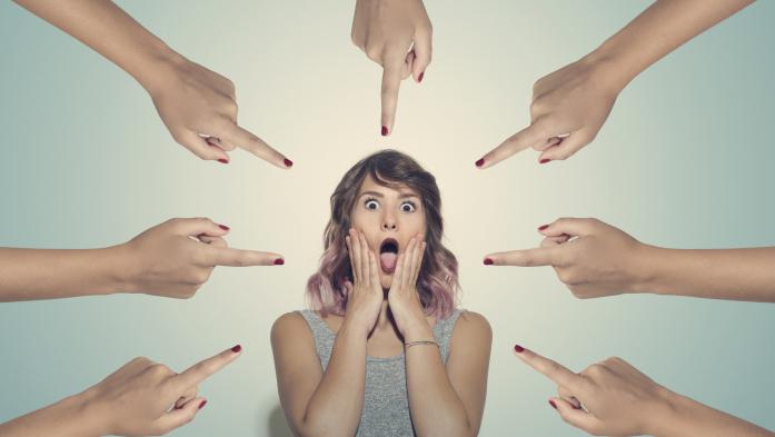 Upset woman surrounded by 7 fingers pointed at her