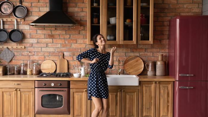Woman dancing  in a kitchen with wood cabinets and dark red appliances
