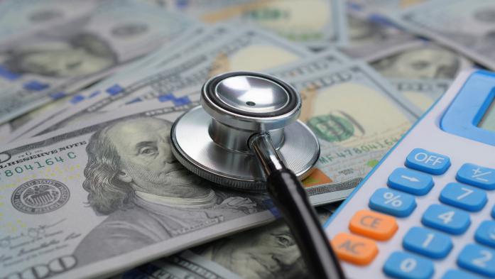 A Stethoscope and calculator on a pile of hundred dollar bills