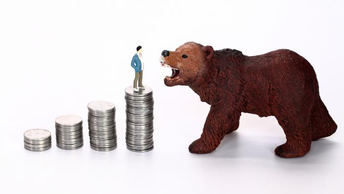 A toy bear growls at a man standing on top of a stack of coins