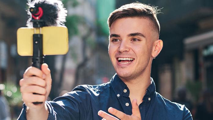 Photo of a young man holding his smartphone on a tripod taking video of himself