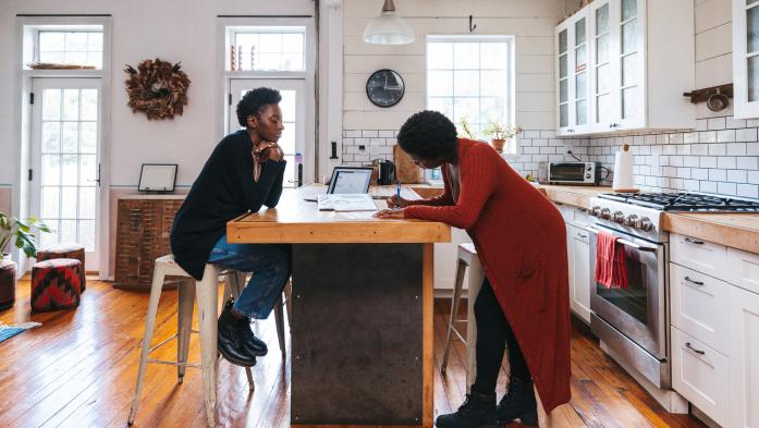 Woman signing paperwork in kitchen with another woman