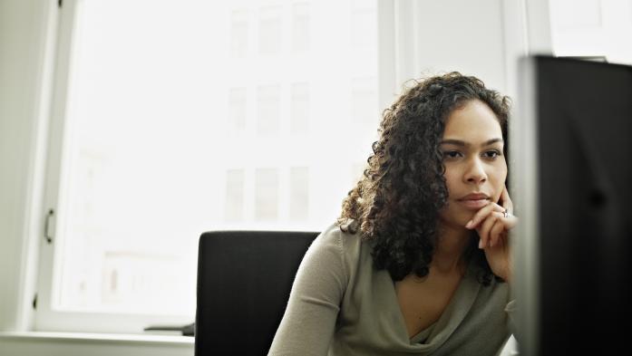 woman with hand to face in front of computer monitor