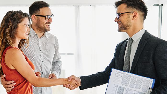 Photo of male realtor shaking the hands of a couple/clients