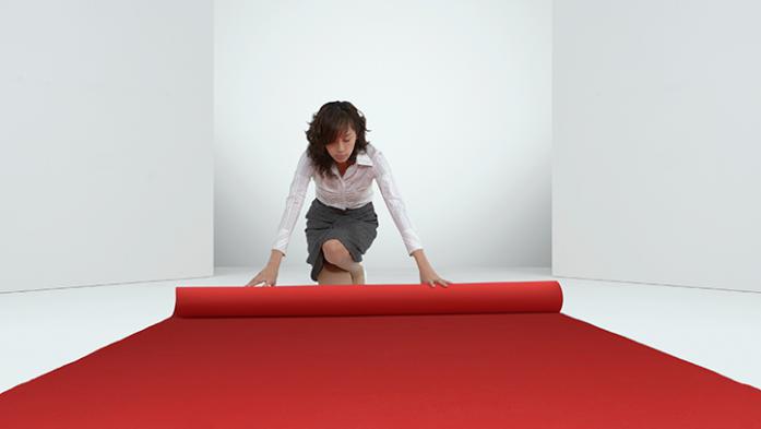 business woman rolling out a red carpet in a white room