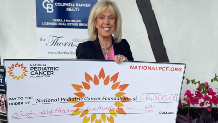 Martha Thorn holds a large version of a $66.5K check for pediatric cancer research 