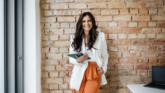 business woman with ipad leaning on brick wall in office