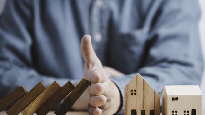 Businessman hand protect and stop wooden house from domino falling wooden bar for risk management and analysis of real estate concept. - stock photo