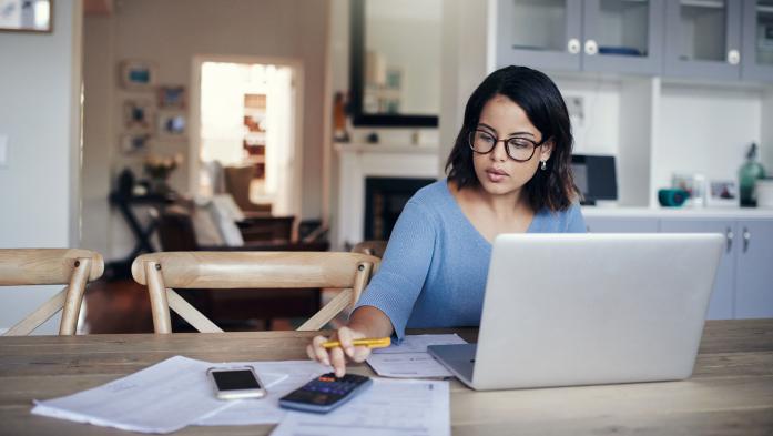 woman using laptop and calculator at kitchen table