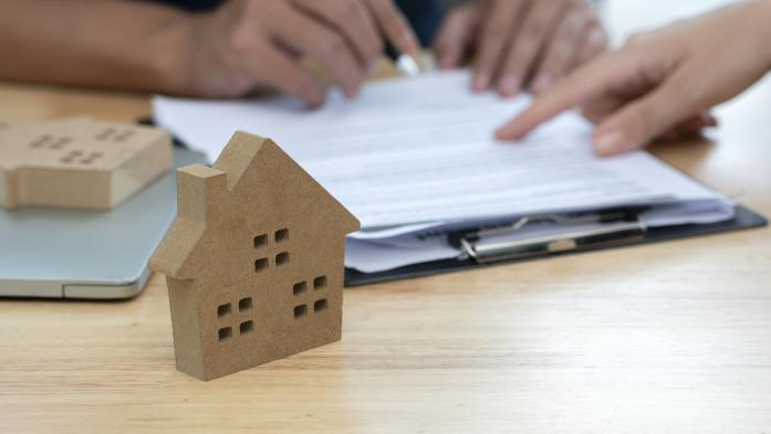 small cardboard house on desk with hands filling out paperwork