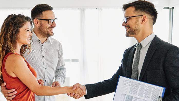 Photo of a male realtor shaking the hands of a couple