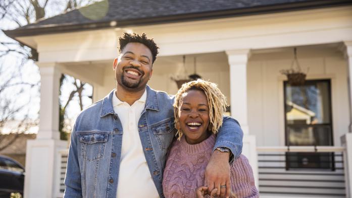 black couple smiling in front of a home 