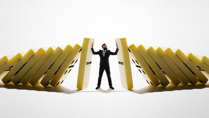 Business man standing in the middle of two sets of dominoes falling with man stopping the falling