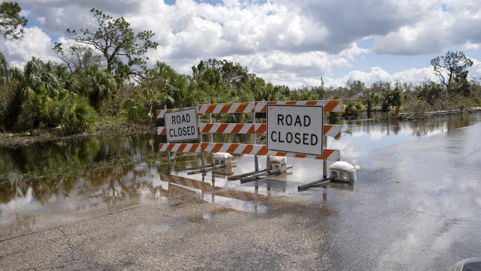 Flooded street in Florida after hurricane rainfall with road closed signs blocking driving of cars. Safety of transportation during natural disaster concept.