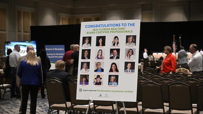 Realtors at Board of Directors meeting with congrats poster of new Board Certified Professionals in front